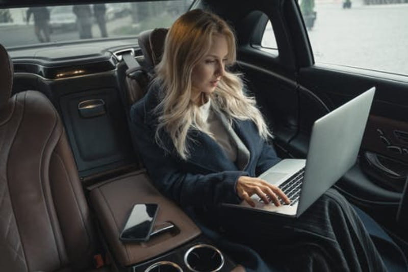 Rich affiliate marketer in her luxury car using a laptop