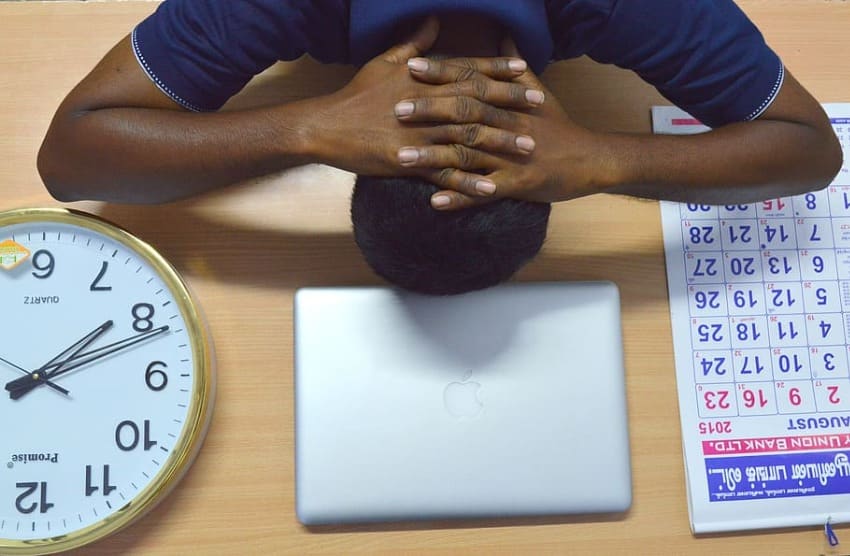 a blogger putting head on table that has a laptop calendar and clock