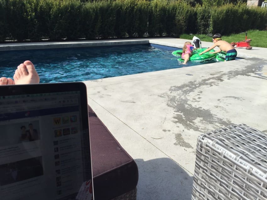 an internet marketer is making money online by the pool with his two kids playing in the water