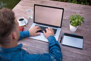 a man blogger writing unique content on his laptop with a cup of coffee and a small pot of flower on the table